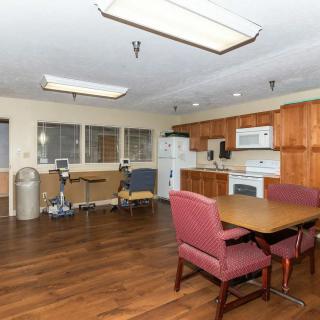 A kitchen and dining area with wooden flooring, featuring a table with chairs, and equipped with appliances like a microwave, refrigerator, and oven.