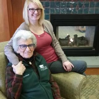 Two women smiling and sitting near a fireplace indoors.