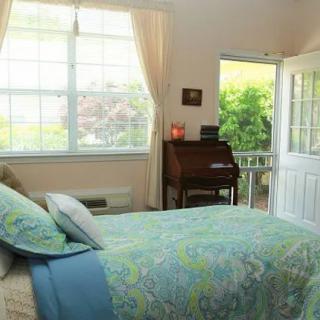 A cozy bedroom with a bed, natural light streaming through a large window, and an open door leading outside.