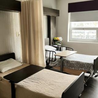 A hospital room with two beds separated by a privacy curtain, featuring a window allowing natural light.