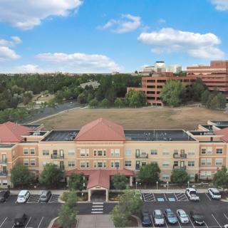 A view of a residential building with a parking lot and trees in the background under a partly cloudy sky.
