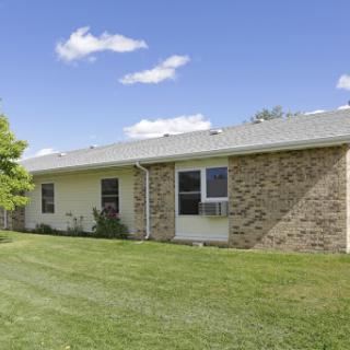 A charming single-story house surrounded by lush green grass and a clear blue sky.