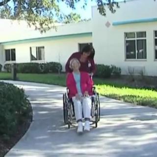 A caregiver assisting an elderly person in a wheelchair along an outdoor path.