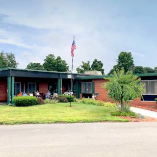 A view of a well-maintained building surrounded by green grass and trees, with the American flag flying.