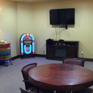 A cozy game room featuring a jukebox, wall-mounted TV, and a round table with chairs.