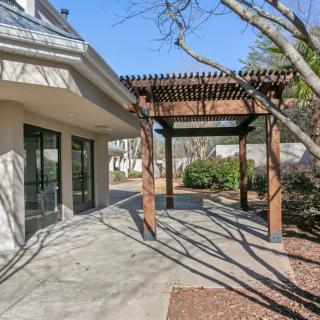 A sunny outdoor patio with a wooden pergola and surrounding trees.