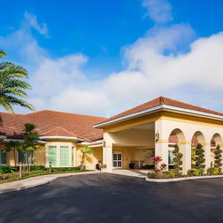 A residential building with a driveway, surrounded by landscaping and a palm tree under a clear blue sky.