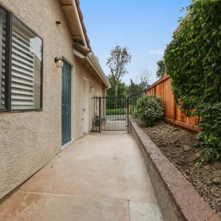 A narrow backyard pathway with a fence and neatly landscaped bushes.