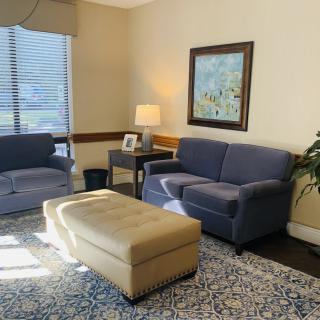 A cozy living room with a blue sofa and armchair, beige ottoman, and warm lighting.