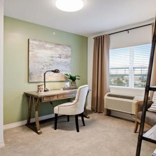 A cozy home office space with a green accent wall, featuring a stylish desk and chair next to a window letting in natural light.