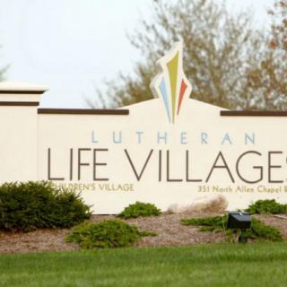 Sign for Lutheran Life Village surrounded by greenery.