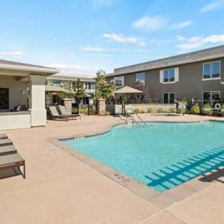 An outdoor swimming pool area in a residential apartment complex with lounge chairs and umbrellas.