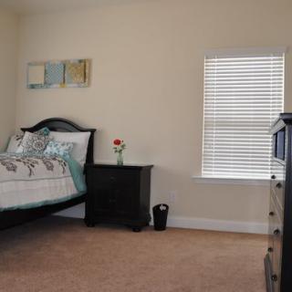 A cozy bedroom with a bed, nightstand, dresser, and window blinds.