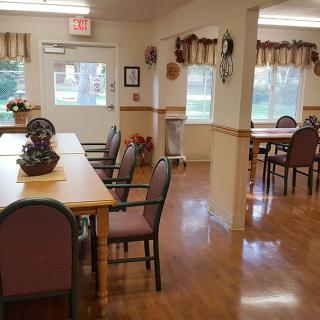 A cozy dining room with neatly arranged tables and chairs, complemented by natural lighting from the windows.