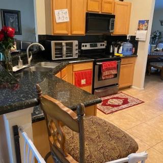 A modern kitchen with wooden cabinets, a stove, microwave, and a countertop with a bar stool.