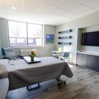 A modern hospital room with a bed, large window, and television.