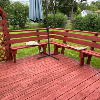 A wooden deck with benches and an umbrella stand in a backyard setting.