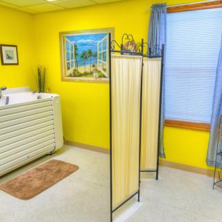 A brightly decorated room with yellow walls, featuring a bathtub and screen partition.