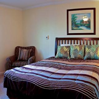 A cozy bedroom featuring a large bed with patterned bedding and pillows, an upholstered chair, and a painting on the wall.