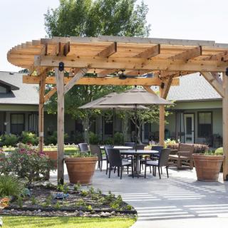 A cozy outdoor patio with a wooden pergola and seating area surrounded by plants.