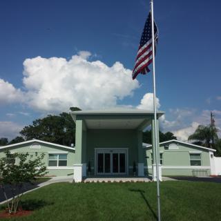 A building with a United States flag on the lawn under a partly cloudy sky.