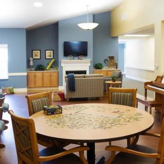 A cozy living room with a round table, chairs, television, and a piano in the background.