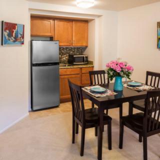 A cozy kitchen and dining area with a table set for four, featuring a bouquet of flowers and modern appliances.