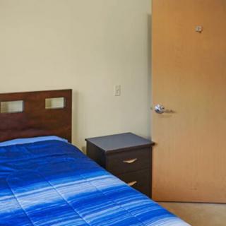 A simple bedroom with a bed, blue blanket, nightstand, and door.