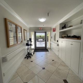 A well-lit hallway with tiled flooring, artwork on the walls, and a glass door leading outside.