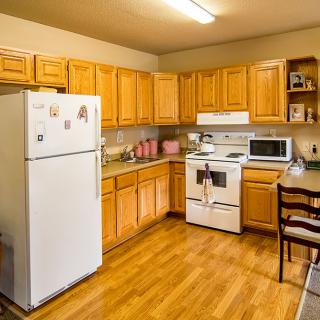 A cozy kitchen with wooden cabinetry, featuring a refrigerator, stove, microwave, and dining area.
