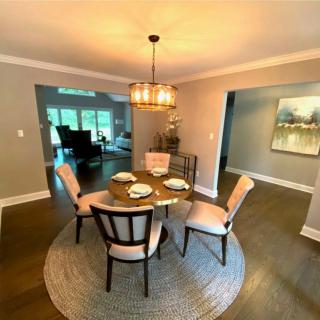 A modern dining room with a round table set under a stylish chandelier, featuring an open layout and contemporary artwork.