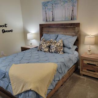 A cozy bedroom featuring a wooden bed with blue bedding and decorative pillows, flanked by matching nightstands and lamps, complemented by wall art.