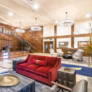 A stylish hotel lobby featuring a red sofa, elegant chandeliers, and wood paneling.