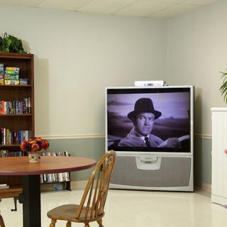 A cozy living room setup featuring a large television displaying a classic black and white film, complemented by a bookshelf and dining furniture.