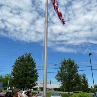 An American flag on a tall flagpole under a partly cloudy sky with trees in the background.