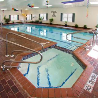 A spacious indoor swimming pool area featuring a jacuzzi and ample seating.