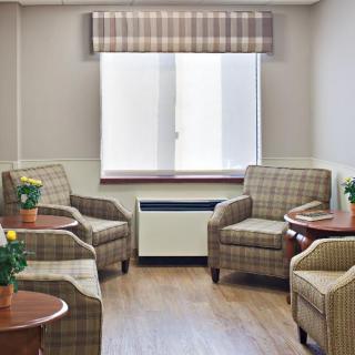 A cozy waiting room with plaid armchairs, small tables, and potted plants near a large window.