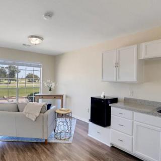 A modern and minimalist living room with an adjacent kitchenette, featuring a large window and wooden flooring.