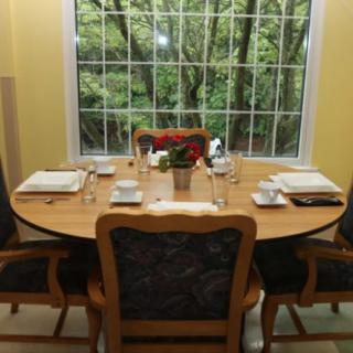 A cozy dining room with a round table set for four, featuring a large window with a view of greenery outside.