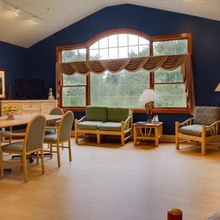 A cozy living room area with large windows, featuring sofas, chairs, and a table.