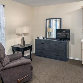 A cozy living room with a recliner, dresser, and a TV.