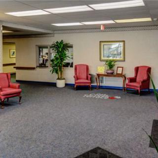 A quiet waiting area with red chairs, a table, and an indoor plant on a carpeted floor.