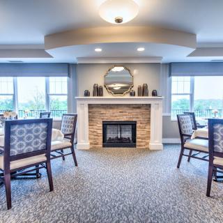 A well-lit dining room with a central fireplace, surrounded by tables and chairs.