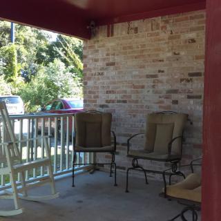 A cozy porch with a couple of chairs and a rocking chair against a brick wall.