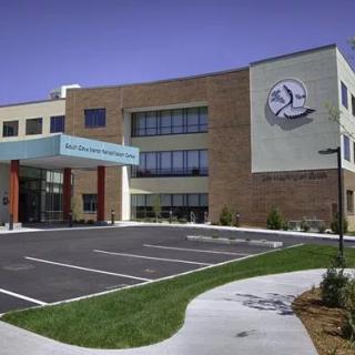An exterior view of a modern hospital building with an entrance and parking area.