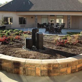 A landscaped garden with a central fountain and a seating area on a patio.