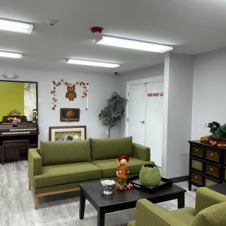 A cozy living room with green sofas and bright lighting, decorated with wall art and indoor plants.