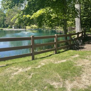 A peaceful pond surrounded by trees and a wooden fence on a sunny day.
