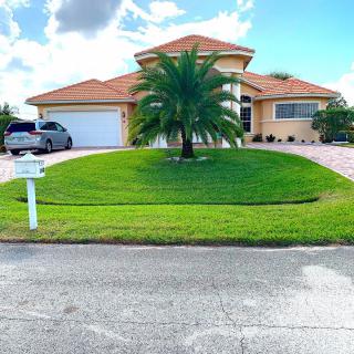 A suburban house with a well-maintained lawn and palm tree in front, featuring a driveway leading to the garage.
