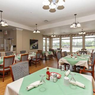 A well-arranged dining area with green tablecloths and neatly set tables, illuminated by elegant lighting fixtures.